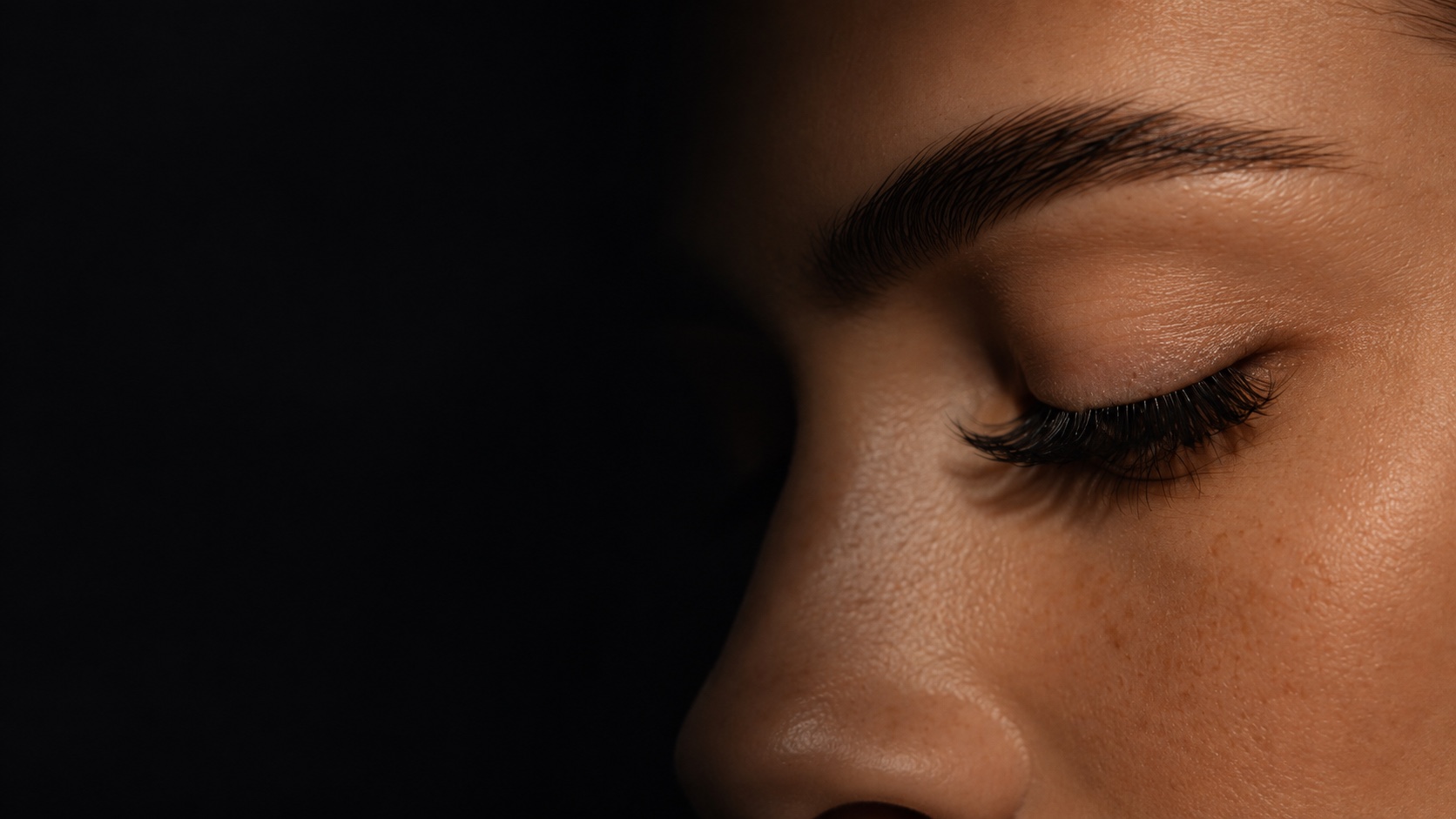 Editorial close-up of a closed eye and brow, fading into shadow
